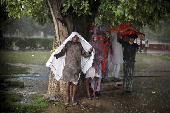नई दिल्‍ली में बारिश के बीच एक पेड़ के नीचे शरण लेता हुआ एक व्‍यक्ति।