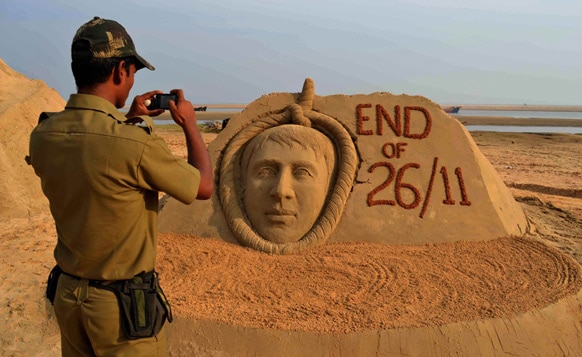 उड़ीसा के बालासोर में कसाब की बनाई रेत की प्रतिमा की फोटोग्राफी करता पुलिसकर्मी।