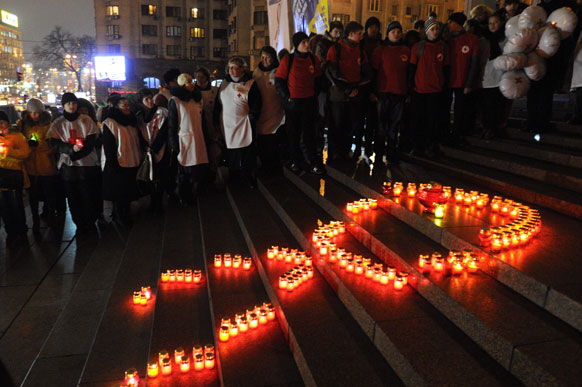 यूक्रेन के किव में विश्व एड्स दिवस पर रेड रिबन की आकृति को मोमबत्ती से सजाते यूक्रेन के लोग।