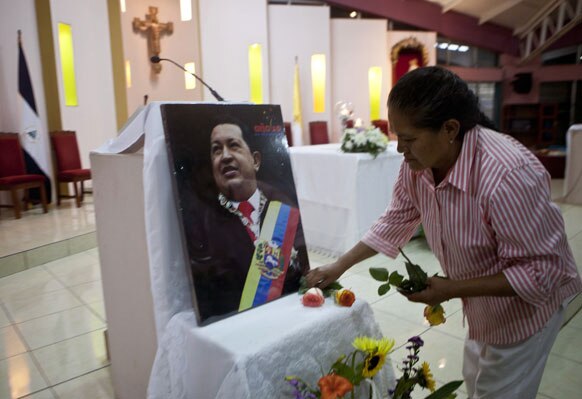 निकारागुआ में वेनेजुएला के राष्‍ट्रपति हूगो शावेज की तस्‍वीर के सामने फूल अर्पित करती हुई एक महिला।