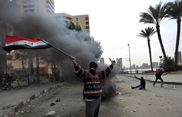 मिस्र के काहिरा में पुलिस-प्रदर्शनकारियों की झड़प के दौरान प्रदर्शनकारी राष्ट्रीय झंडे के साथ प्रदर्शन करते हुए।
