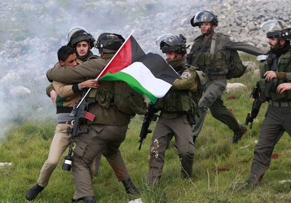 पश्चिमी तट पर एक फलीस्तीनी प्रदर्शनकारी को हिरासत में लेते इजरायल के सुरक्षाकर्मी।