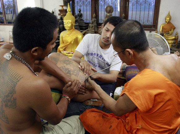 बैंकाक में एक व्यक्ति की पीठ पर टैटू बनाता एक बौद्ध भिक्षु।