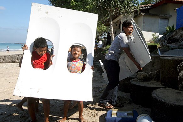 इंडोनेशिया के बाली में जिंबारन बिच के दुर्घटनाग्रस्त विमान के टुकड़े को ले जाते हुए बच्चे।