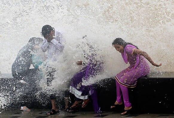 मुंबई में समंदर किनारे बारिश का मजा लेते लोग।