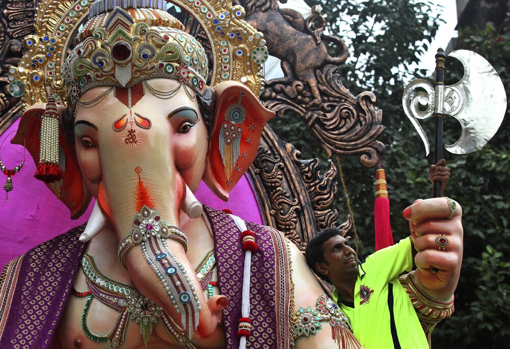 मुंबई में गणेश चतुर्थी पर्व के मद्देनजर नवनिर्मित भगवान गणेश की मूर्ति के हाथ में फरसा को सही तरीके से व्‍यवस्थित करता एक कलाकार।