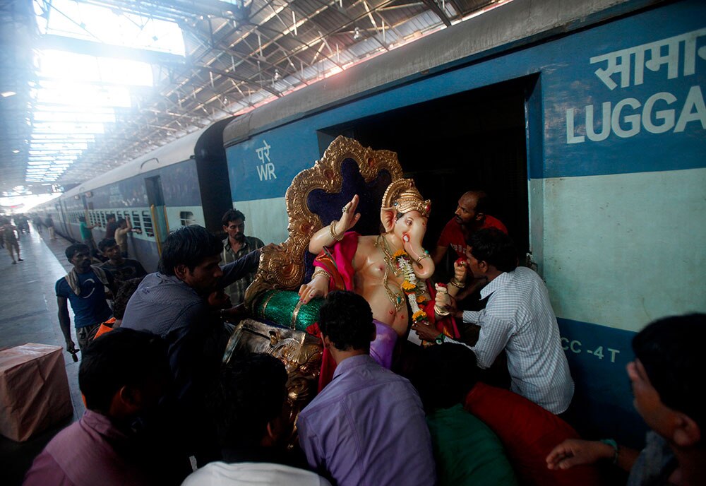 मुंबई में गणेश चतुर्थी पर्व के मद्देनजर भगवान गणेश की मूर्ति को एक पैसेंजर ट्रेन से पूजा स्‍थल की ओर ले जाते हुए श्रद्धालु।