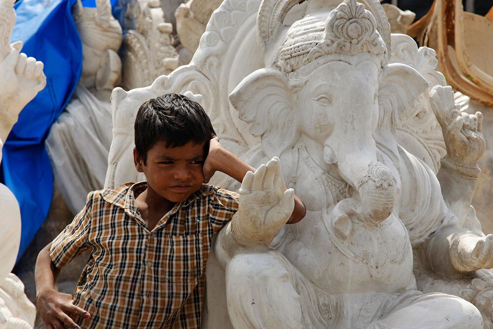 हैदाराबाद में गणेश चतुर्थी पर्व के मद्देनजर भगवान गणेश की निर्मित प्रतिमा के सामने खड़ा एक बालक।