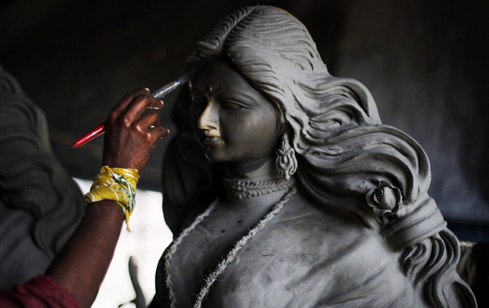 नई दिल्ली में दुर्गा पूजा की प्रतिमा को आकार देने के बाद रंगों से रंगता एक पेंटर।