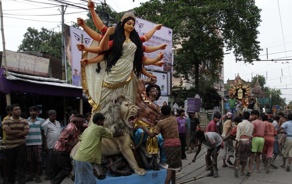 कोलकाता की सड़कों पर मां दुर्गा की विशाल प्रतिमा को ले जाते लोग।