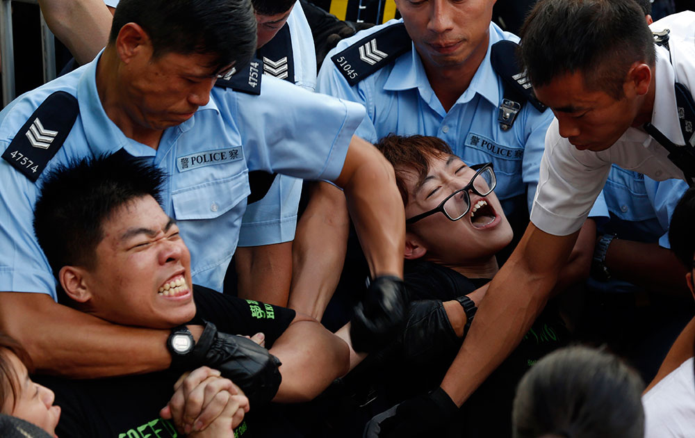 हांगकांग के एक वाणिज्यिक जिले की गलियों में शांतिपूर्ण प्रदर्शन कर रहे लोगों को हटाते हुए पुलिसकर्मी।