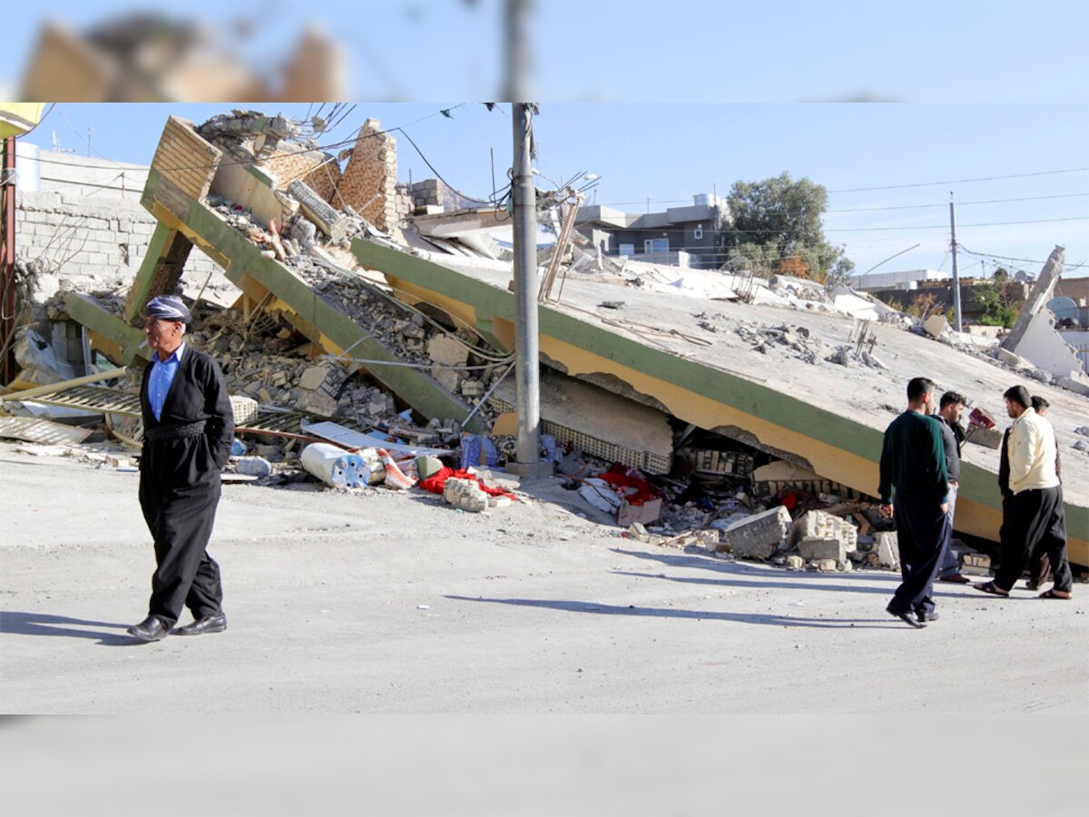 ईरान में आए भीषण भूकंप के बाद वहां के एक शहर में गिरी इमारत के सामने से गुजरते लोग. (Reuters/14 Nov, 2017)