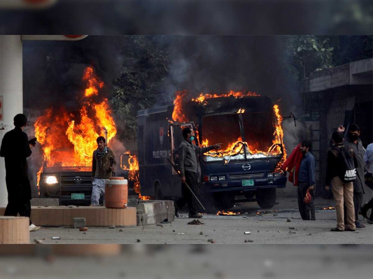 इस्लामाबाद में हिंसक झड़प के बाद जले हुए पुलिस वाहन के पास जमा पाकिस्तानी प्रदर्शनकारी. (फोटो- PTI)